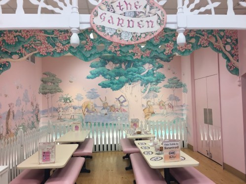 A whimsical café interior with pink walls, a mural of trees and animals, and reserved tables in a charming setting.