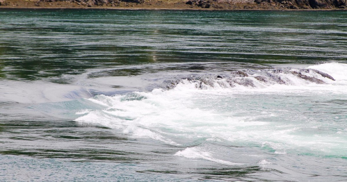 Waves gently lap against rocky shoreline in a serene body of water, reflecting light and creating ripples.