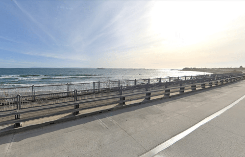 A serene beach view with gentle waves, a paved walkway, and a clear sky in the background.