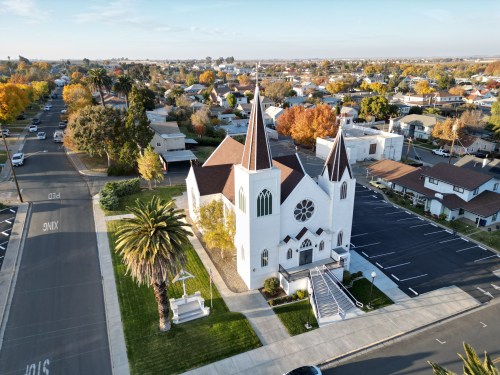 Aerial view of a white church with spires, surrounded by colorful autumn trees and residential buildings.