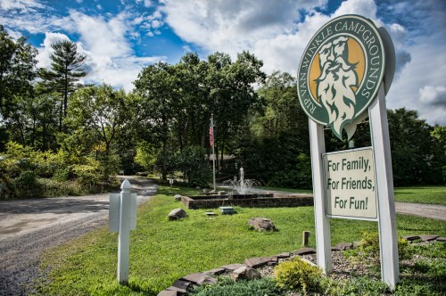 Sign for a campground surrounded by trees, with a fountain and a clear blue sky in the background.