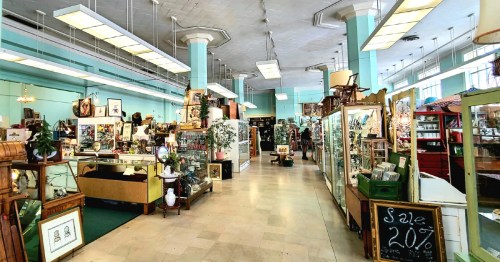 A spacious vintage shop filled with various antiques, displays, and a sale sign for 20% off.