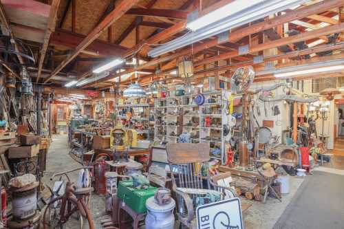 A cluttered workshop filled with various tools, antiques, and collectibles under bright overhead lights.