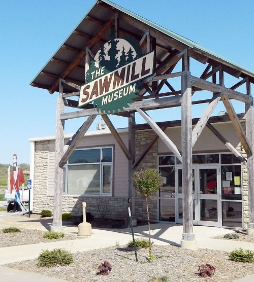 Exterior of The Sawmill Museum, featuring a wooden sign and landscaped entrance on a clear day.