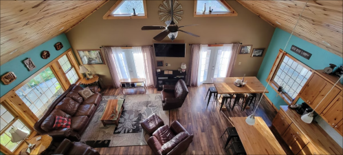 A spacious, cozy living area with leather sofas, wooden accents, and large windows, featuring a dining table and kitchen.