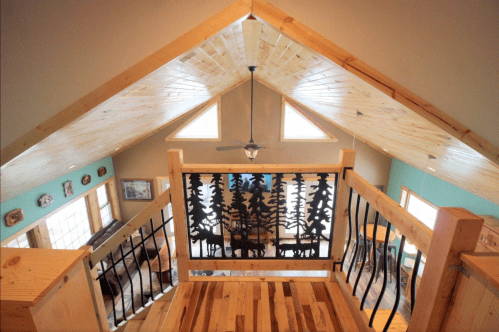 View from a loft overlooking a cozy living space with wooden accents and a decorative railing featuring tree silhouettes.