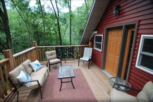 Cozy outdoor deck with seating, a glass table, and views of lush green trees.