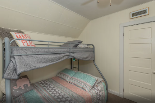 A cozy bedroom featuring a bunk bed with gray bedding and a colorful patterned bottom bed, plus a white door.