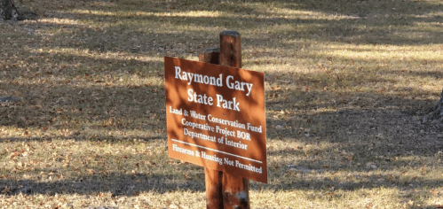 Sign for Raymond Gary State Park, noting conservation efforts and restrictions on firearms and hunting.