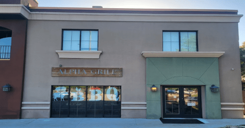 Exterior of a restaurant named "Alpha Grille," featuring large windows and a BBQ sign.