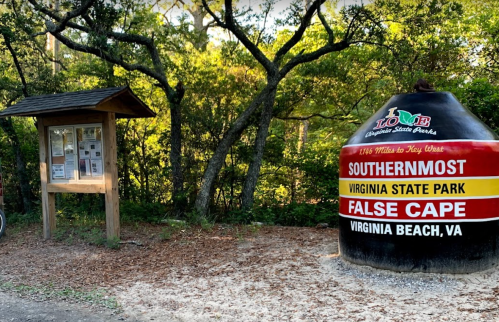 Signpost and large marker for False Cape State Park in Virginia Beach, surrounded by trees and nature.