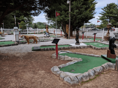 A mini-golf course featuring animal sculptures, flags, and green putting areas surrounded by trees.