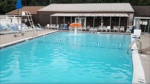A clear blue swimming pool with a diving board, lounge chairs, and a water feature in a sunny outdoor setting.