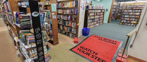 A cozy library interior with bookshelves, a welcome mat, and a sign to watch your step.