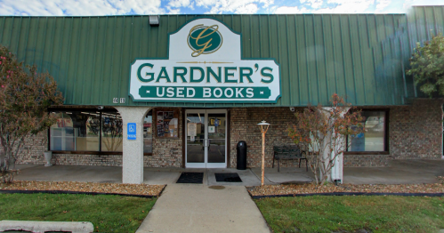 Exterior of Gardner's Used Books store, featuring a green roof and sign, with a welcoming entrance and seating area.