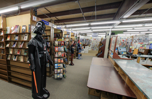 A life-sized Darth Vader figure stands in a bookstore aisle filled with books and magazines.
