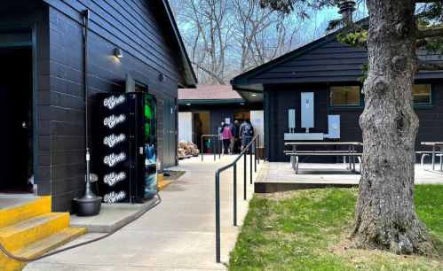 A pathway leads to two buildings, with a vending machine in front and people walking towards the entrance.