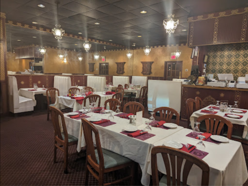 Interior of a restaurant with neatly set tables, white tablecloths, and elegant decor, featuring warm lighting and a cozy atmosphere.