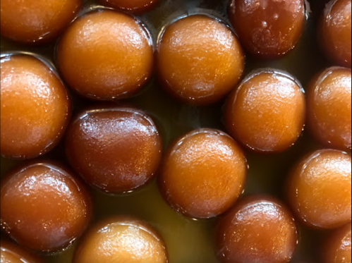 Close-up of round, golden-brown sweets glistening in syrup, arranged closely together.