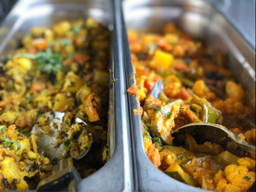 Two trays of colorful vegetable dishes, one with mixed vegetables and the other with a spiced cauliflower and pepper mix.