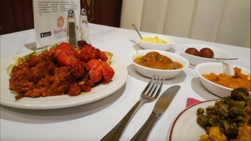 A table set with Indian dishes, including chicken, curries, and desserts, alongside utensils and condiments.