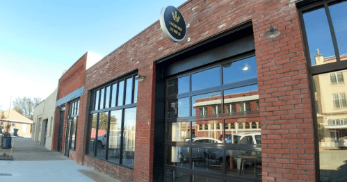 Exterior of a brick building with large windows and a round sign, showcasing a modern storefront in a sunny urban setting.