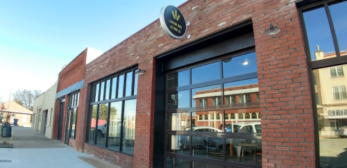 Exterior of a brick building with large windows and a round sign, showcasing a modern storefront in a sunny urban setting.