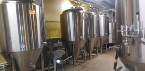A row of shiny stainless steel fermentation tanks in a brewery setting.