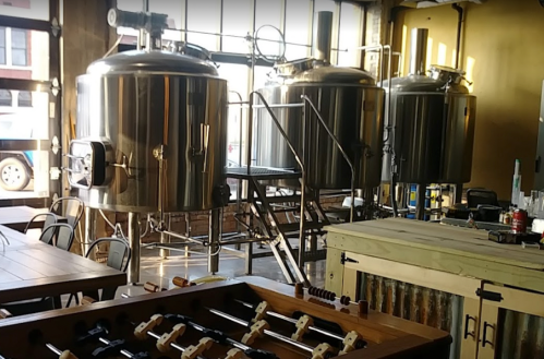 Interior of a brewery featuring large brewing tanks and a foosball table in a casual setting.