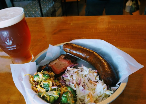 A plate with smoked sausage, brisket, coleslaw, and a side of broccoli, accompanied by a glass of amber beer.