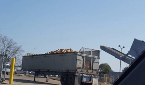 A truck loaded with large bags or containers parked at a loading area under a clear blue sky.