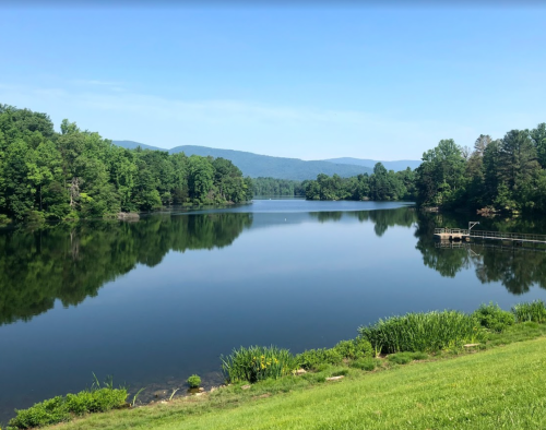 A serene lake surrounded by lush greenery and mountains under a clear blue sky, reflecting the landscape in calm waters.
