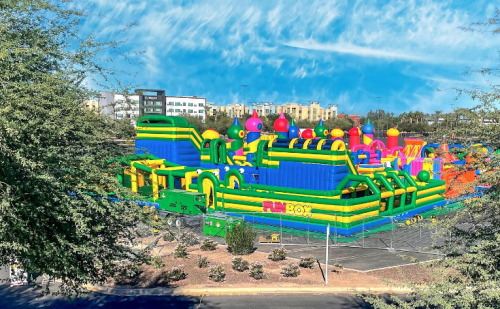 A colorful inflatable bounce house park with various structures set in an outdoor area under a blue sky.