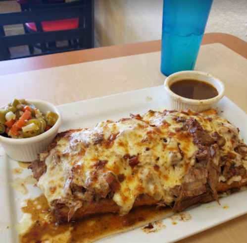 A plate of enchiladas topped with cheese, served with a side of salsa and a small bowl of mixed vegetables.