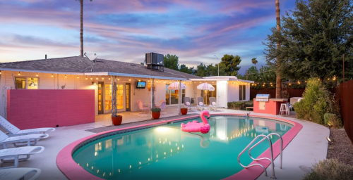 A vibrant pool area at sunset, featuring a pink flamingo float, lounge chairs, and string lights.