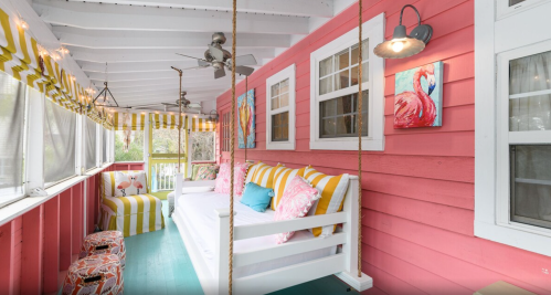 Brightly colored porch with swing seating, striped cushions, and vibrant artwork on pink walls. Cozy and inviting atmosphere.