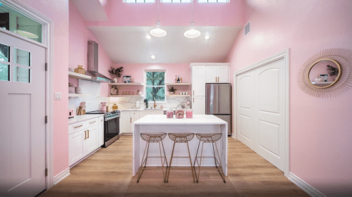Bright pink kitchen with white cabinetry, a central island, and modern appliances, featuring stylish bar stools.