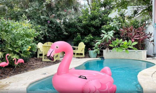A pink flamingo float in a pool surrounded by lush greenery and tropical plants.