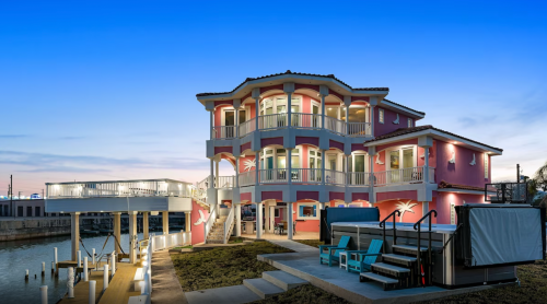 A colorful waterfront house with multiple balconies, surrounded by water and a clear blue sky at dusk.