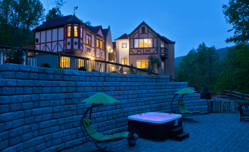 A cozy house with large windows at dusk, featuring a hot tub and lounge chairs in a serene outdoor setting.