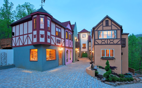 Charming European-style buildings with colorful facades and a cobblestone pathway, surrounded by greenery at dusk.