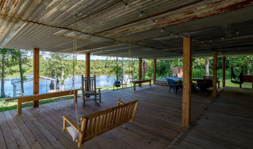 A rustic porch with a swing, overlooking a serene lake surrounded by trees.