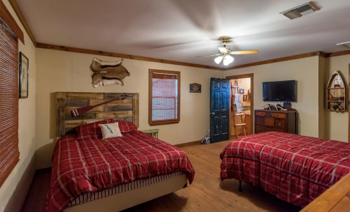 Cozy bedroom with two red plaid beds, wooden accents, a ceiling fan, and a door leading to another room.