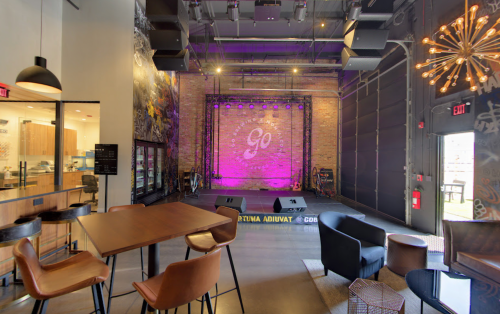 A modern venue with a stage, purple lighting, and seating areas, featuring a brick wall and industrial decor.