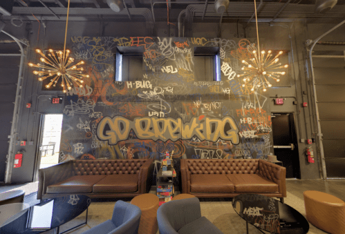 A modern lounge with brown leather sofas, a graffiti wall saying "GO BREWING," and stylish light fixtures.