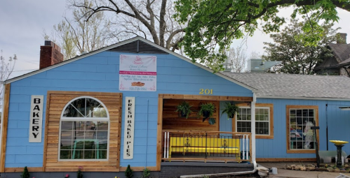 A charming blue bakery with wooden accents, featuring a sign for fresh baked pies and a welcoming porch.