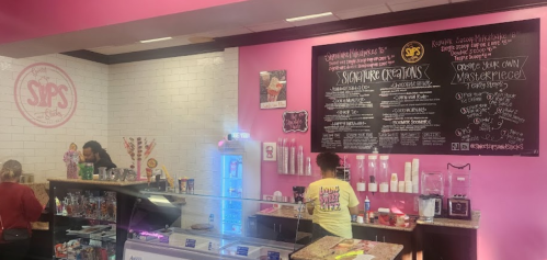 A colorful café interior with a menu board, staff serving customers, and a display of drinks and snacks.
