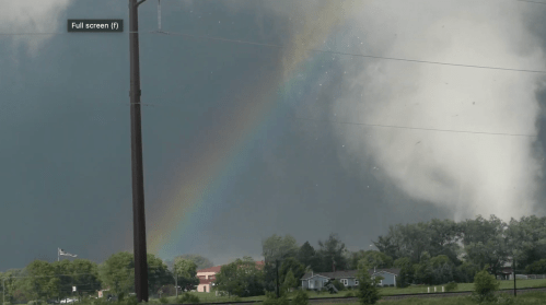 A dramatic sky with dark storm clouds and a vibrant rainbow arching over a rural landscape.