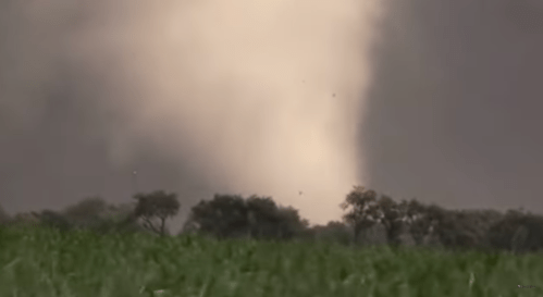 A tornado forming over a field, with dark clouds and trees in the foreground.