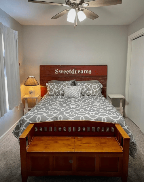 Cozy bedroom featuring a gray and white patterned bedspread, a wooden bench, and a "Sweetdreams" headboard.